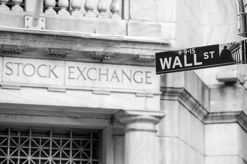 Znak Wall Street widoczny przed New York Stock Exchange na czarno-białym ujęciu dzielnicy finansowej Manhattanu.